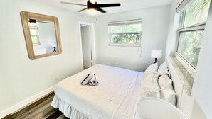 A bedroom with a bed, a ceiling fan, a window, and a mirror.