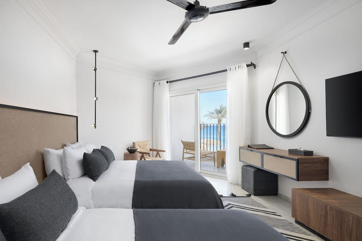 A modern bedroom with a large bed, a desk, and a balcony with a view.