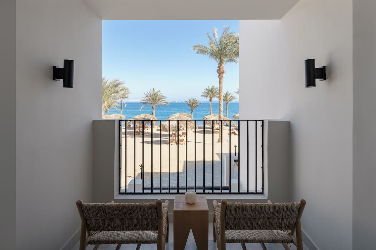 A balcony with two wicker chairs, a small table, and a view of the beach and ocean.