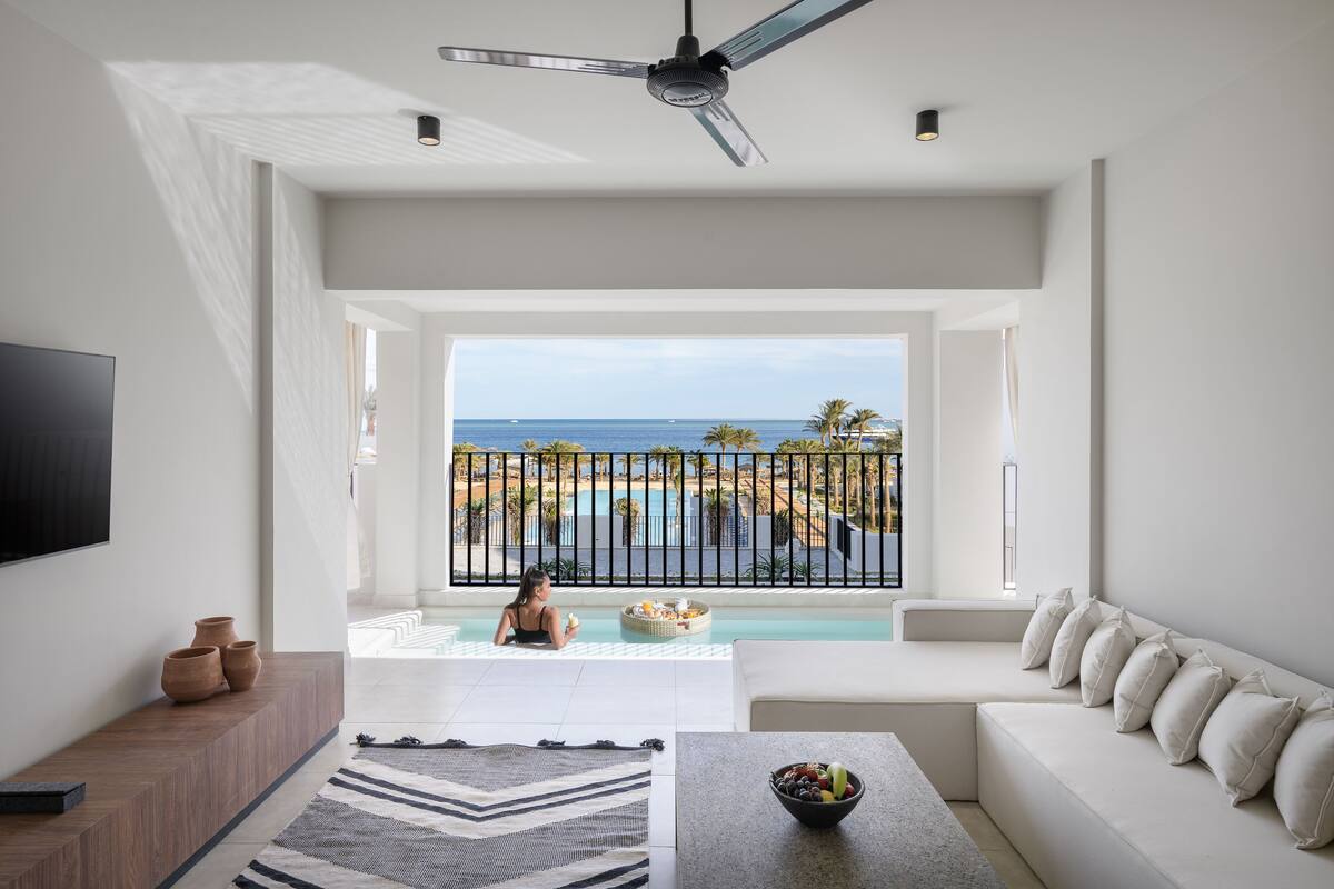 A modern living room with a large window overlooking a pool and ocean view.