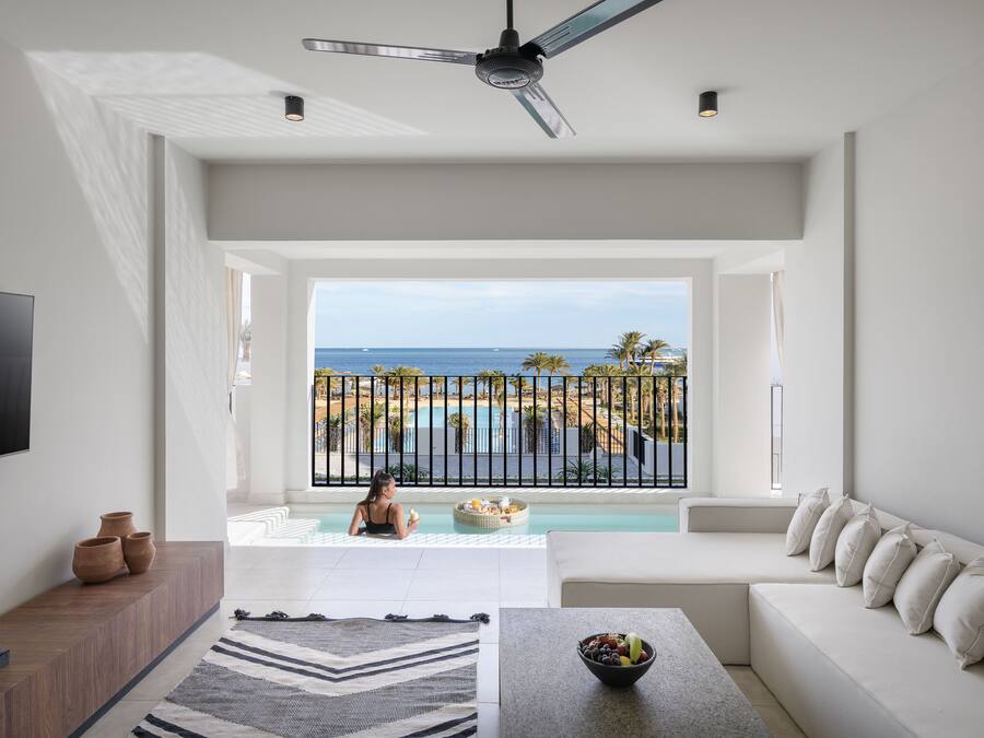 Ein modernes Wohnzimmer mit großem Fenster und Blick auf Pool und Meer.