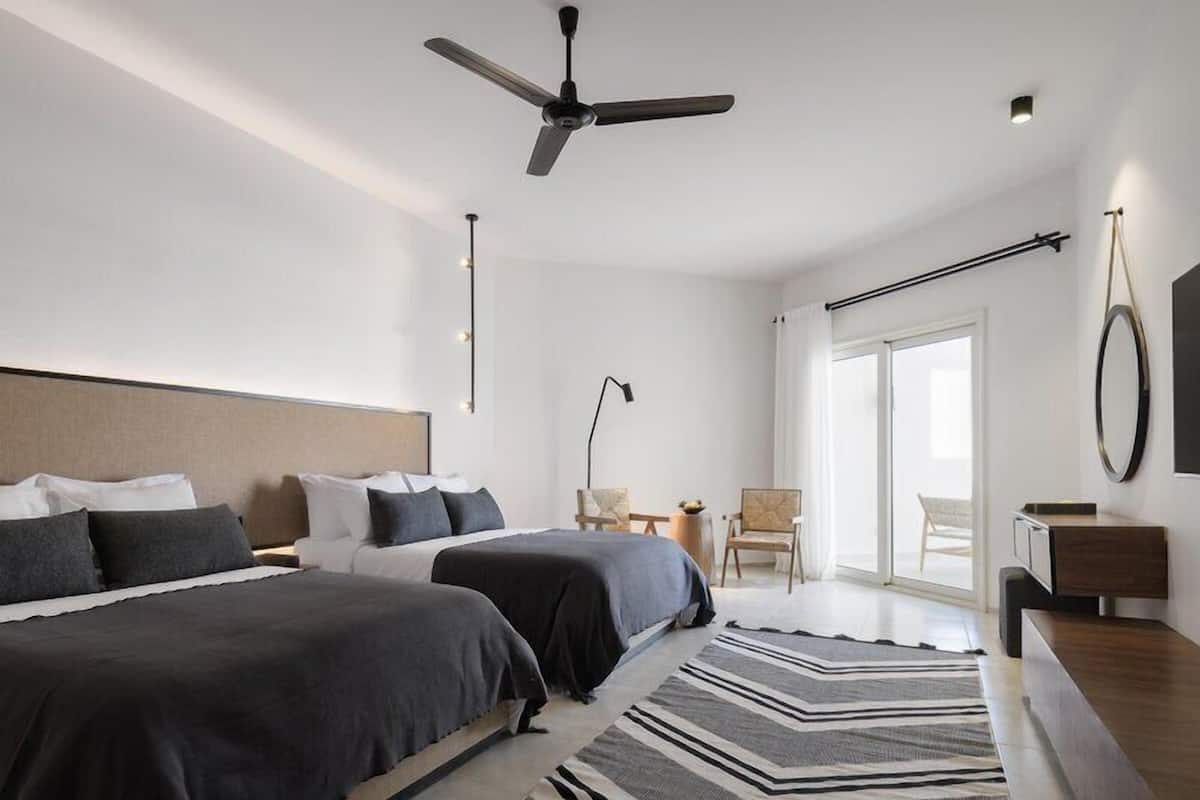 A modern bedroom with two beds, a ceiling fan, a large window, and a view of the outdoors.
