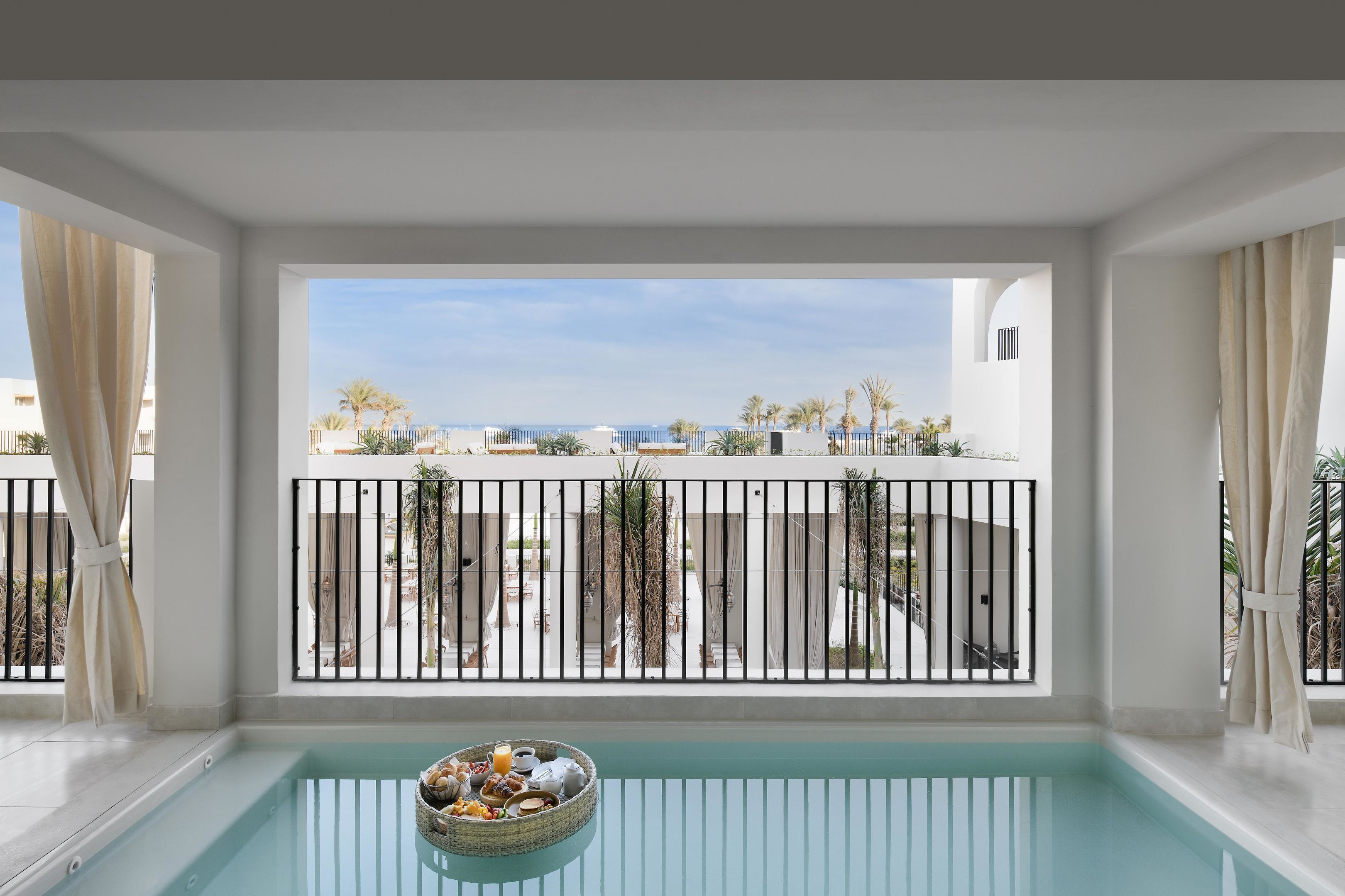 A balcony with a pool, a view of the sea, and a basket of fruits and bottles.