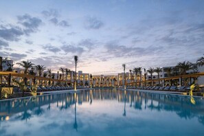 A large pool with lounge chairs and palm trees, surrounded by hotel buildings. - Serry Beach Resort (Hurghada)