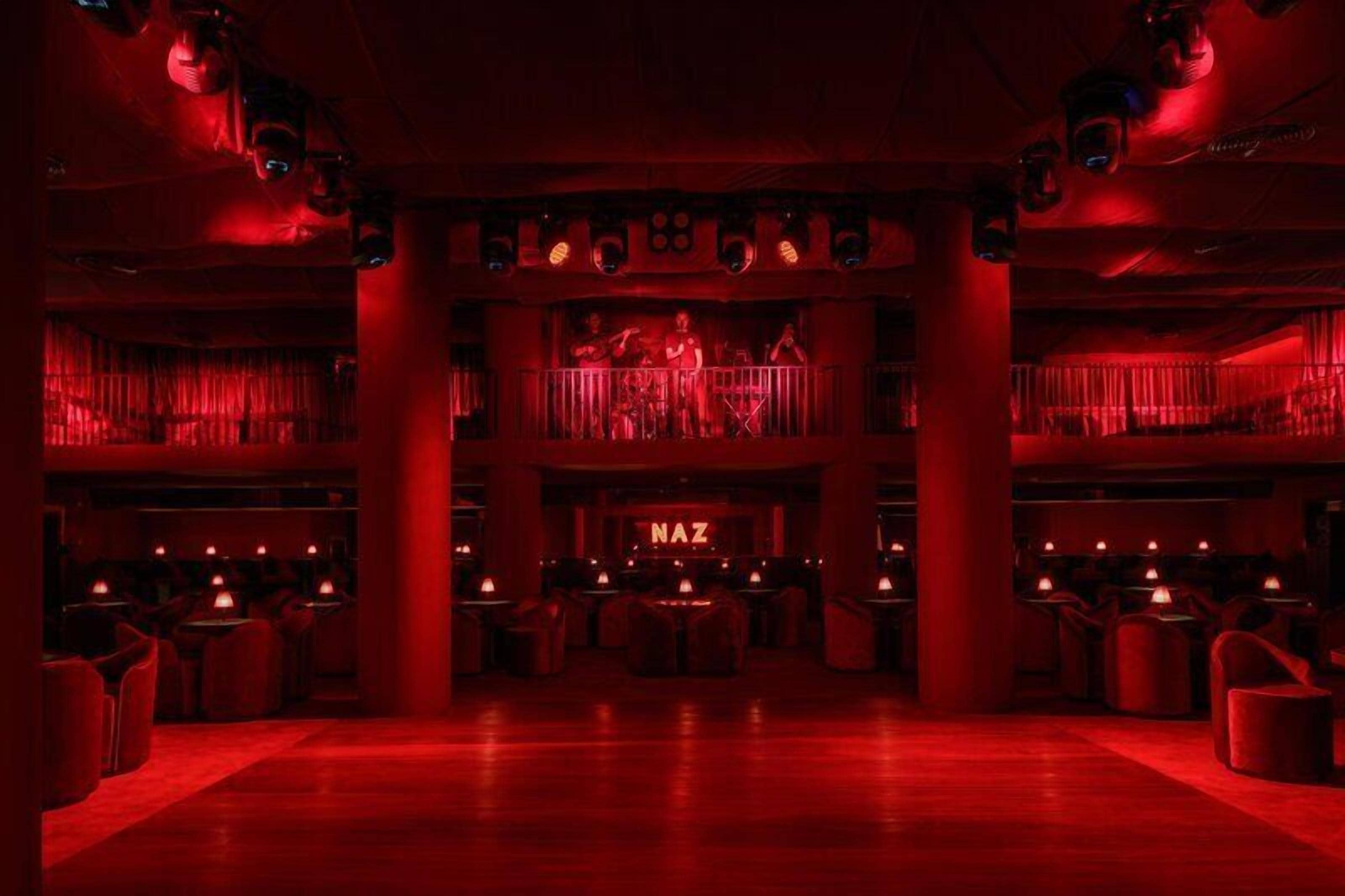 A bar with a neon sign, multiple tables, and a stage with a band.