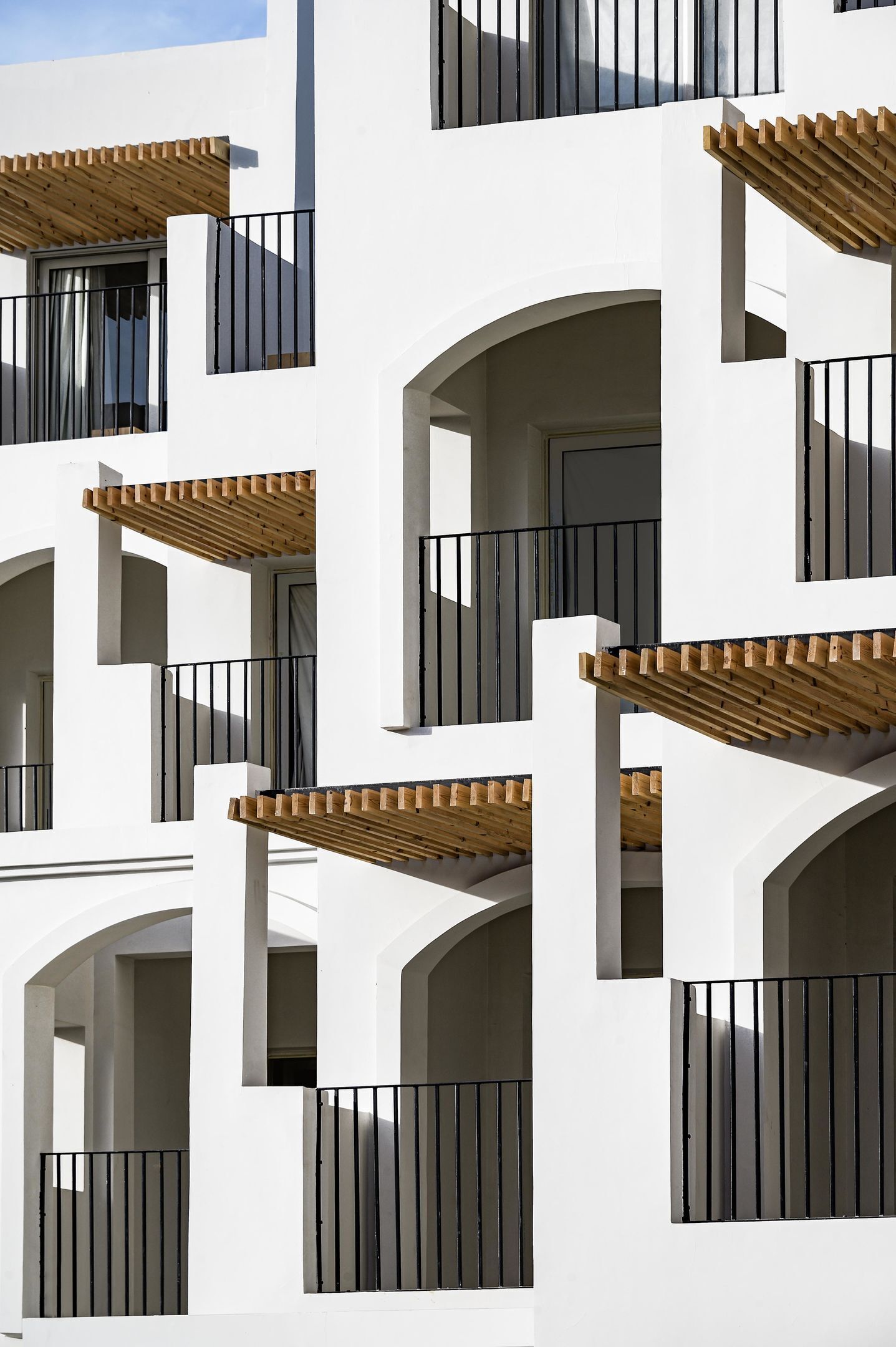 Un edificio moderno con varios balcones, cada uno con pérgolas de madera y barandales negros.