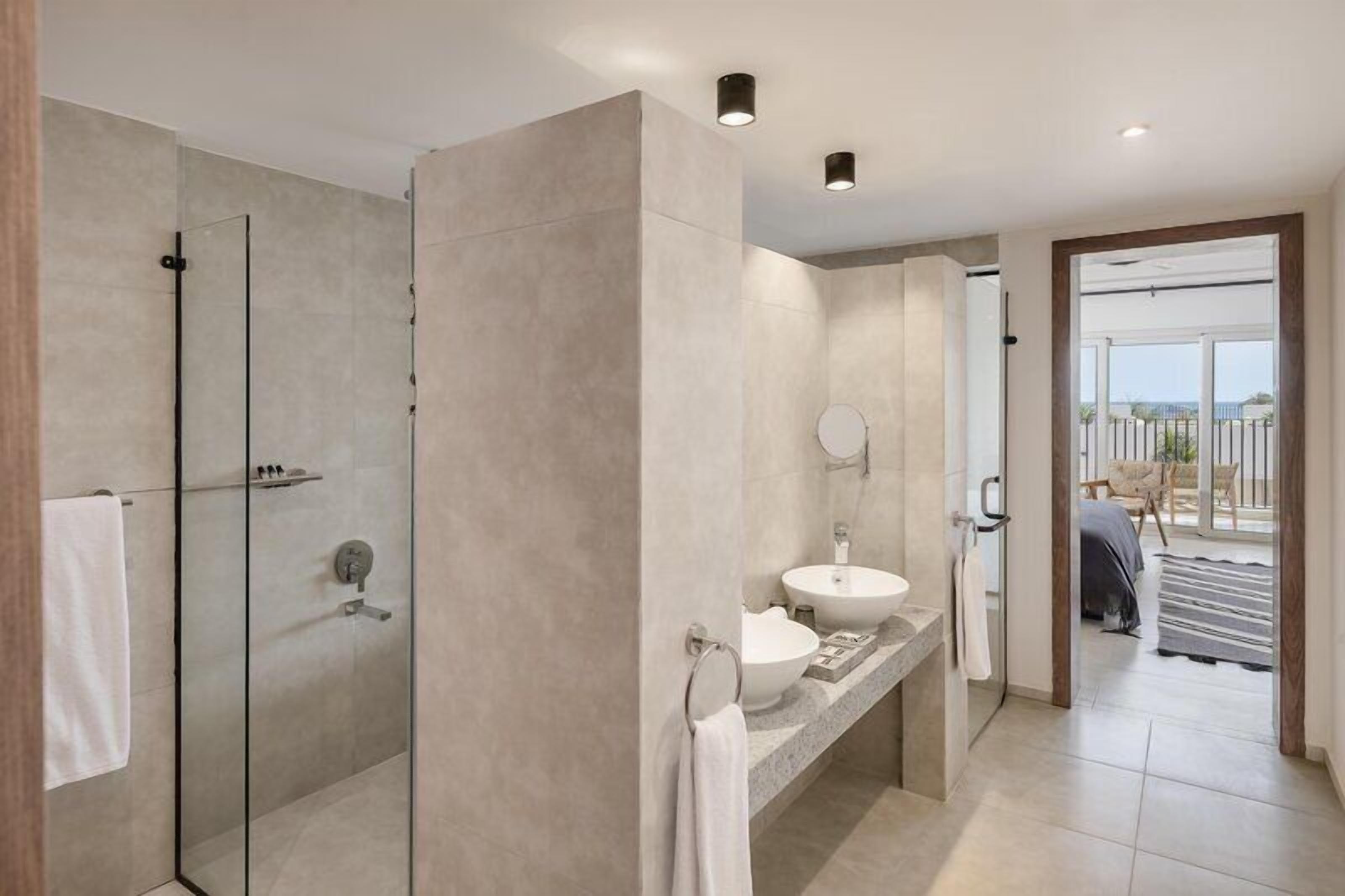A modern bathroom with a glass shower enclosure, a vanity with a sink, and a view of the outdoor area.