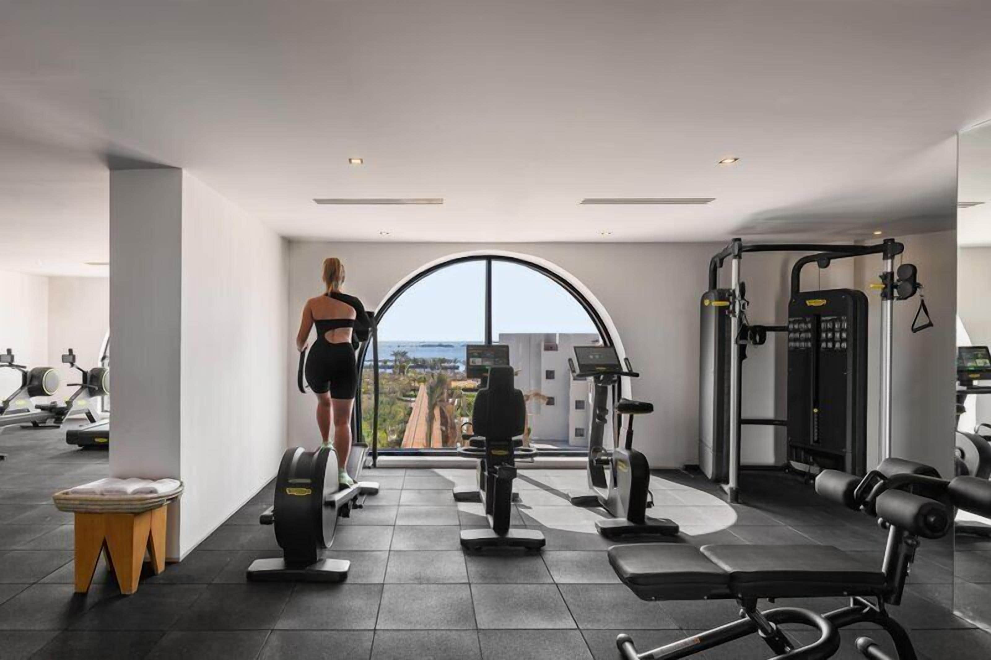 A modern gym with exercise equipment, a large window, and a view of the city.
