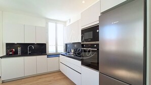 Una cocina moderna con armarios blancos, encimera negra, microondas Bosch y refrigerador de acero inoxidable.