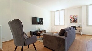 Una sala de estar moderna con un sofá gris, un sillón gris y un televisor de pantalla plana montado en la pared.
