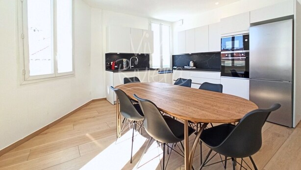 Una cocina moderna con una mesa y sillas de madera, electrodomésticos de acero inoxidable y armarios blancos.