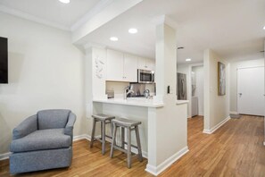 A modern kitchen with white cabinetry, a microwave, and a refrigerator. There are two stools at the kitchen island. - Beachy & Beautiful Renovated Villa Just Steps from (Hilton Head Island)