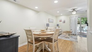 A dining area with a round wooden table, white chairs, and a ceiling fan. - Beachy & Beautiful Renovated Villa Just Steps from (Hilton Head Island)