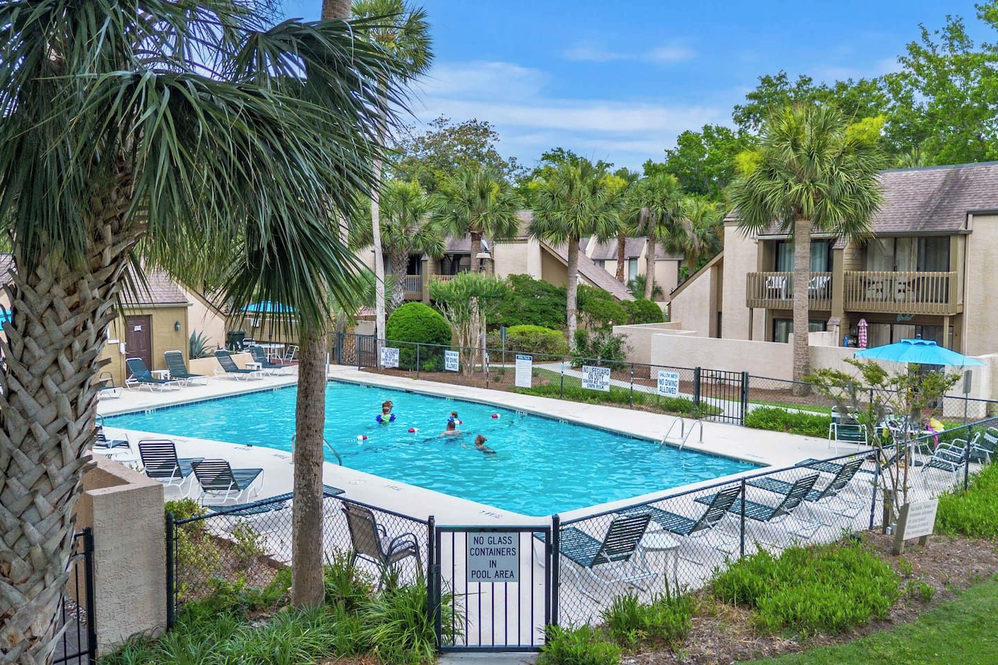A swimming pool with lounge chairs and palm trees, surrounded by a fence.