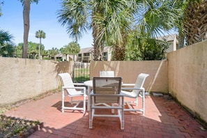 An outdoor patio with a table and chairs, surrounded by a high wall and palm trees.