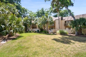 A residential building with multiple balconies, surrounded by a well-maintained lawn and various trees. - Beachy & Beautiful Renovated Villa Just Steps from (Hilton Head Island)