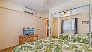 A bedroom with a bed, a television on a small table, a ceiling fan, and a window with curtains. - Ocean View Sleeps 8 Across from Beach 3 bedroom 3 bathroom Full AC Kihei Condo  (Kihei)