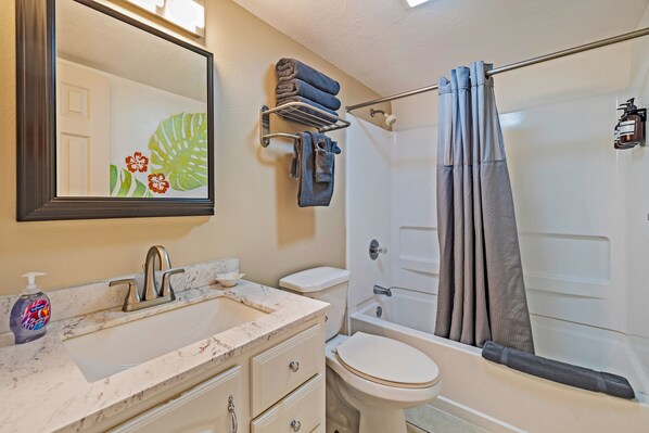 A bathroom with a sink, toilet, and bathtub. There is a towel rack with folded towels and a shower curtain.