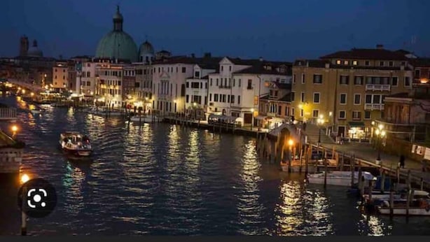 Vista nocturna de un canal bordeado por edificios, un puente y barcos.