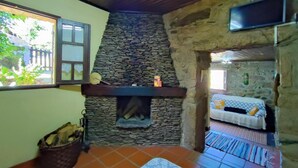 A rustic room with a stone fireplace, a bed with a patterned bedspread, and a window with a view of greenery outside.