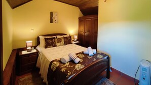 A bedroom with a wooden ceiling, a bed with floral bedding, a nightstand with a lamp, and a wardrobe.
