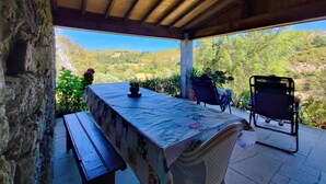 A covered outdoor seating area with a table and chairs, overlooking a hilly landscape.