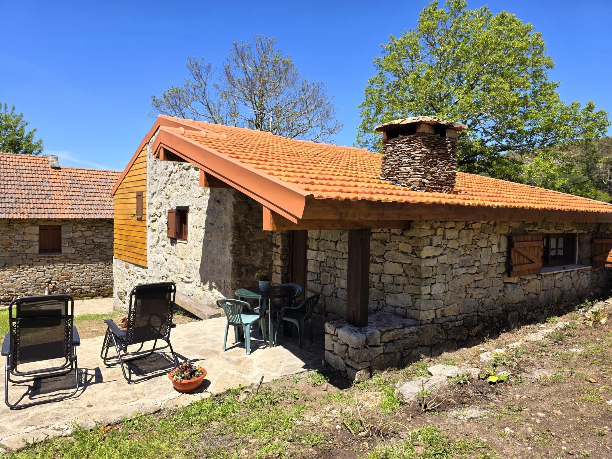 Ein Steinhaus mit einem Ziegeldach, Außenbestuhlung und einem kleinen Tisch mit Stühlen.