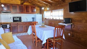 Una camera accogliente in stile chalet con tavolo da pranzo, sedie di legno, divano, angolo cottura completo di microonde e frigorifero, e TV a parete.