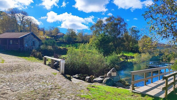 Un sentiero in pietra conduce a un rustico edificio in pietra con un terrazza in legno affacciata su un fiume.