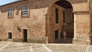 Un edificio de piedra con tejado de tejas, un arco de entrada y una ventana pequeña con un escudo de armas.
