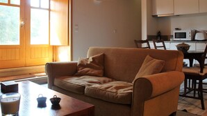 Een gezellige woonkamer met een bank, een tafel met een kaars, en een keukenhoek met een magnetron en kastjes.