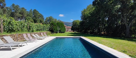 A rectangular swimming pool with clear blue water, surrounded by a stone wall and a grassy area with trees.