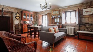 Una sala de estar acogedora con un sofá, sillas de mimbre, una mesa de comedor y una zona de cocina con armarios de madera y una pared de piedra.