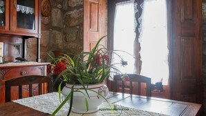 Una mesa de comedor de madera con una servilleta blanca, una planta en maceta con flores rojas y una pared de piedra al fondo.