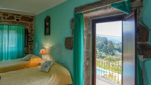 A bedroom with two beds, a nightstand with a lamp, and a view of a balcony with a pool.