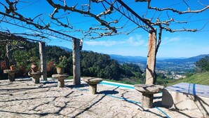 A stone patio with rustic stone tables and planters, overlooking a scenic landscape with mountains and a clear sky.