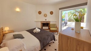Ein Schlafzimmer mit Bett, Nachttisch, Kommode, Kamin und Blick ins Freie.