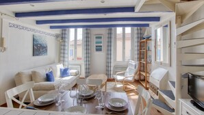 A dining area with a wooden table set for four, a white sofa, and a television on a stand.