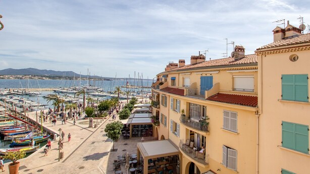 A coastal marina with boats, a café, and buildings with balconies.