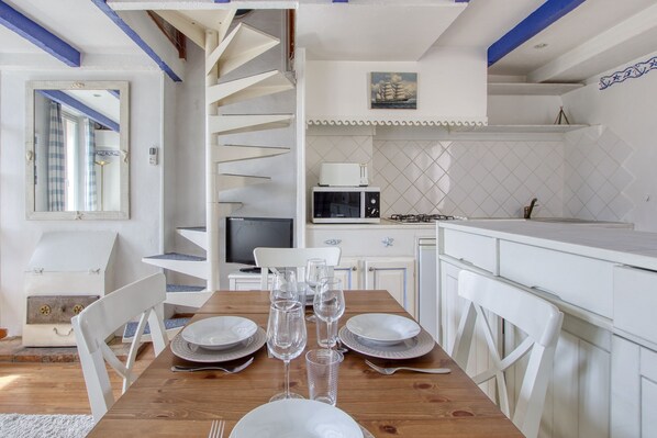 A dining area with a wooden table set for four, white chairs, and a white cabinet with a microwave.