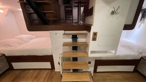 Een compacte kamer met twee bedden, een houten trap en een klein zitgedeelte.