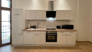 A modern kitchen with white cabinets, a stainless steel range hood, a built-in oven, and a window providing natural light. - Bamboo City (Magdeburg)