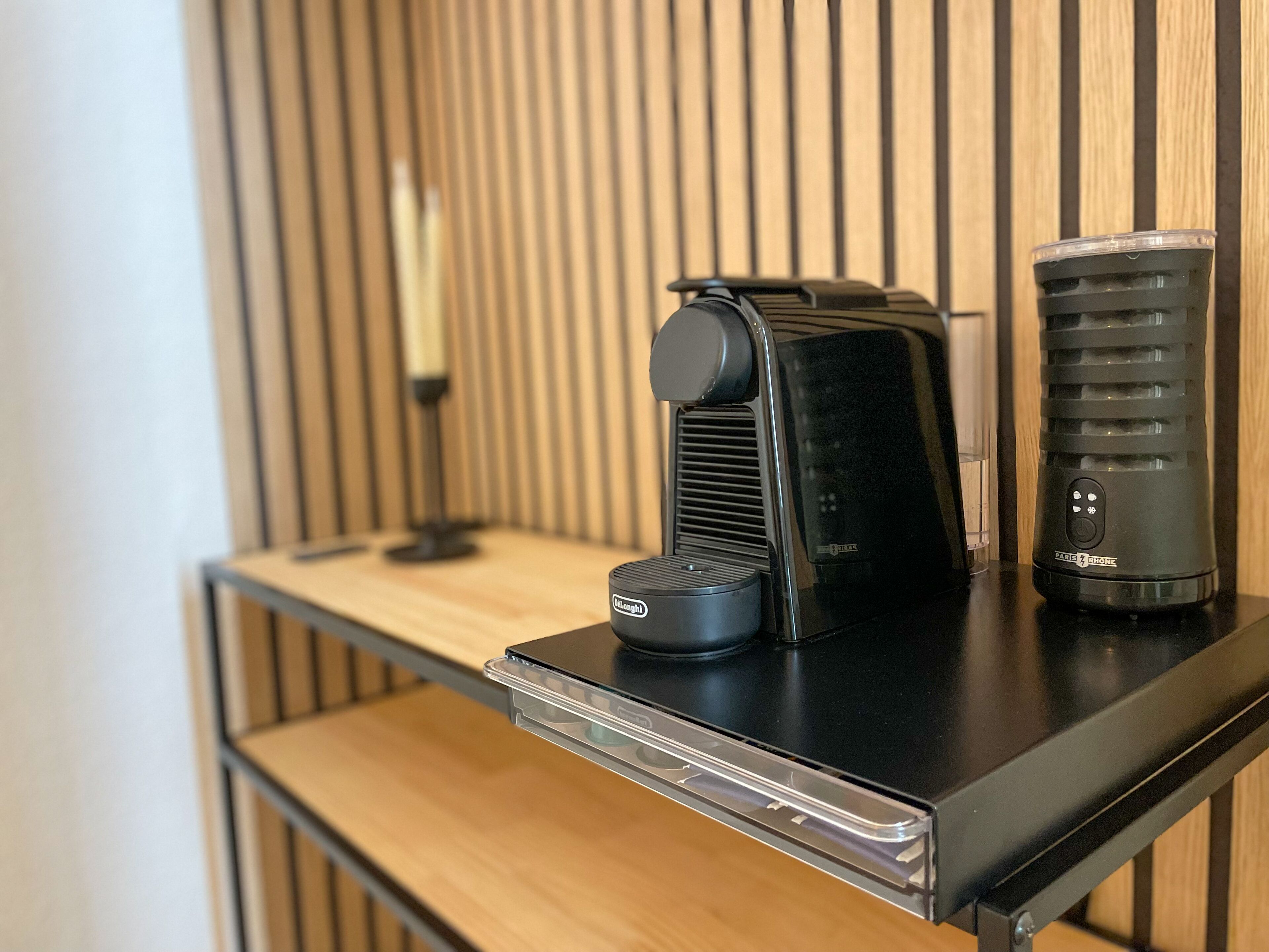 A coffee maker and a water dispenser on a black countertop with a wooden panel background.