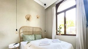 A bedroom with a wooden bed, a bedside table, a window with curtains, and a potted plant. - Bamboo City (Magdeburg)