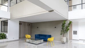 A spacious, modern lobby with a glass coffee table, two yellow chairs, a blue sofa, and a potted plant. - LUXURY STUDIO (Cali)