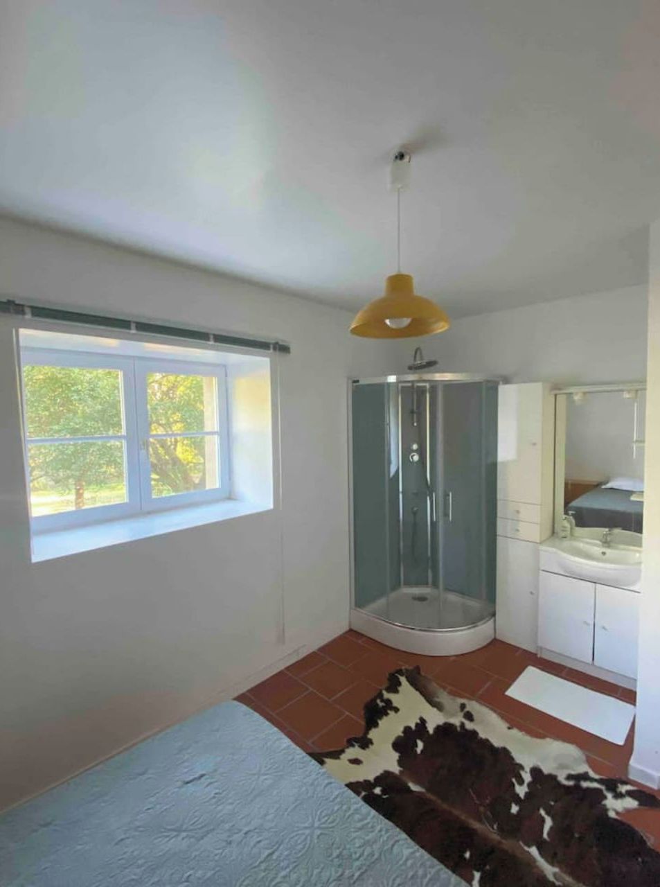 Un bagno con box doccia in vetro, un lavandino e una finestra vista alberi.