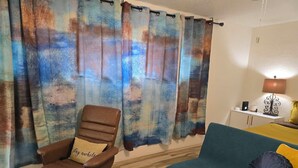 A room with a brown leather chair, a teal sofa with a yellow pillow, and a white table with a lamp.