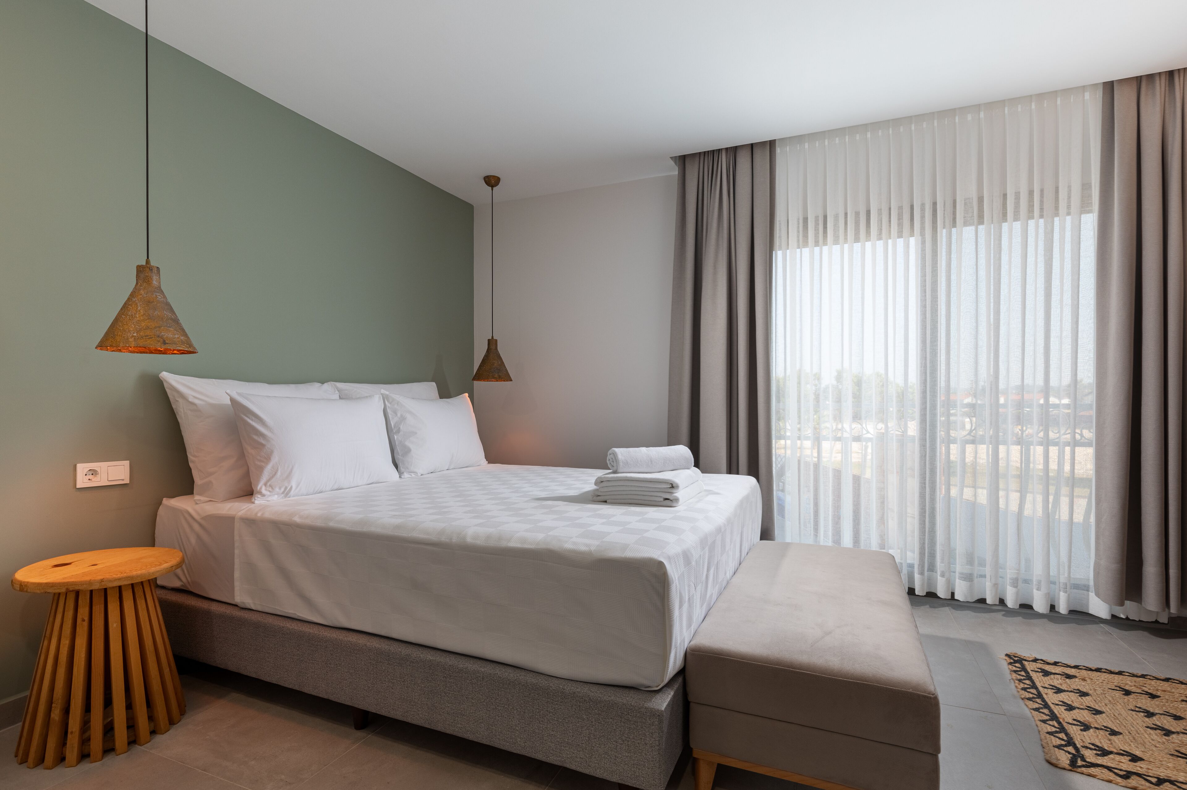 Quarto de hotel moderno com uma cama grande, um banquinho de madeira e um banco.