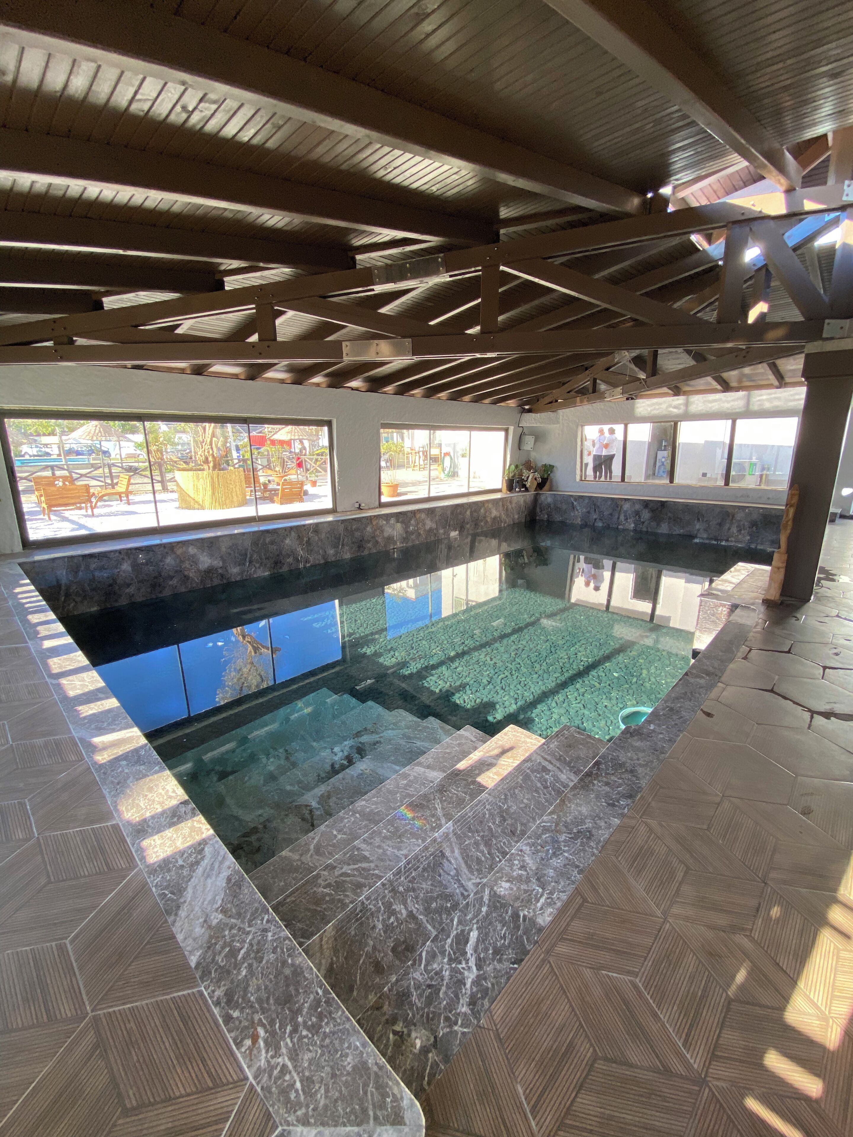 Piscina interna con acqua cristallina, circondata da pavimentazione piastrellata e ampie finestre.