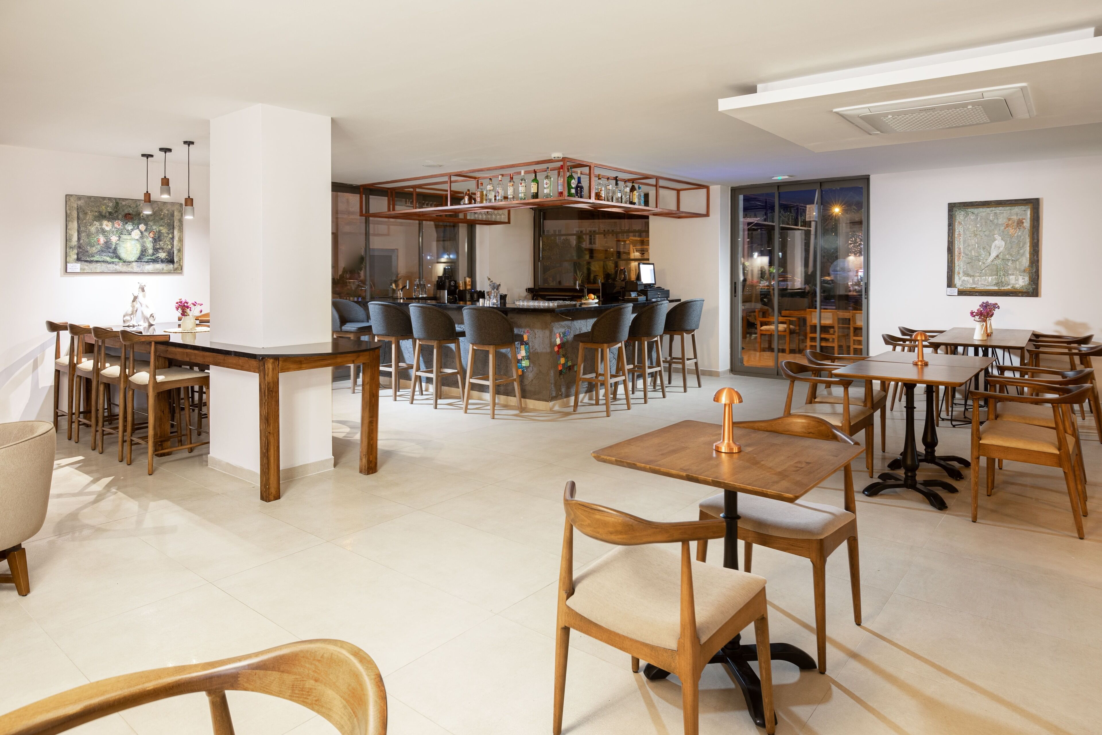 A modern restaurant with a bar area, wooden furniture, and large windows.